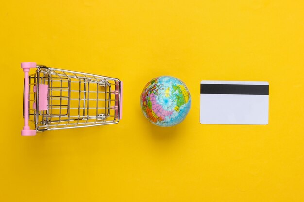 Tema de compras. Carrinho de supermercado com globo, cartão de crédito na superfície amarela. Vista do topo