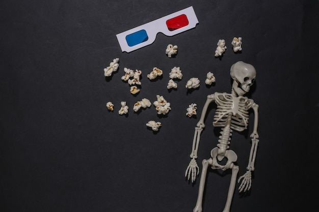 Tema de Halloween. Esqueleto, pipoca e óculos 3d em um fundo preto. Filme de terror. Vista do topo