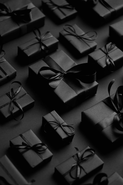 Tema de Natal escuro Presentes em caixas quadradas embrulhadas em papel preto e fita dispostas em fundo preto Vista superior plana