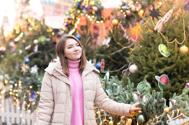 Tema de Natal. Linda jovem Europeia em um fundo de uma árvore de Natal, luzes e brinquedos com um humor alegre, feliz, sonhos de presentes.