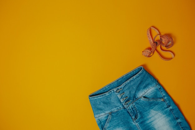 Tema de dieta y pérdida de peso. Blue jeans y cinta métrica naranja con espacio de copia.