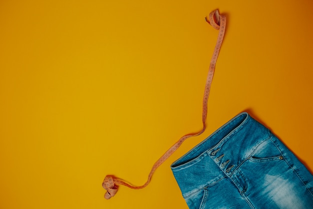 Tema de dieta y pérdida de peso. Blue jeans y cinta métrica naranja con espacio de copia.