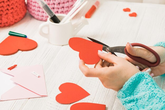 Tema do dia dos namorados Mãos femininas cortam o coração do papel Ferramentas de presentes embalados em uma mesa de madeira maltratada Local de trabalho para a preparação de ornamentos artesanais