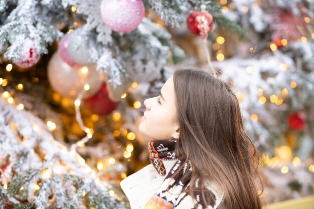 Tema navideño. Joven hermosa chica europea sobre un fondo de un árbol de Navidad, luces y juguetes en un estado de ánimo alegre, feliz, sueños de regalos.