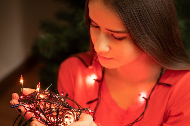 Tema navideño. Una mujer joven está sosteniendo luces en sus manos, sonriendo, a punto de decorar un árbol