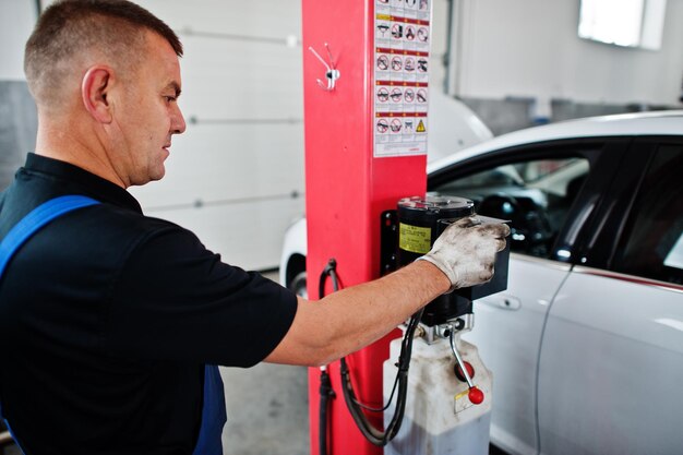 Tema de reparación y mantenimiento de automóviles Mecánico en uniforme que trabaja en el servicio automático presione el botón para levantar el automóvil