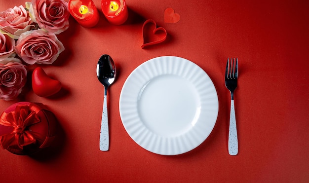 Tema rojo del día de San Valentín con platos blancos vacíos, cucharas, corazón de papel, velas y flores.