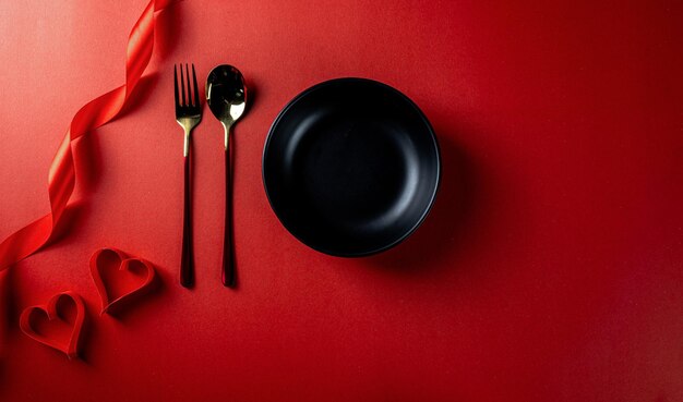 Tema rojo del día de san valentín con platos negros vacíos con cuchara, corazón de papel y cinta