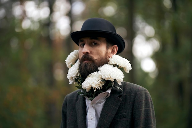 El tema surrealista un hombre barbudo con una chaqueta y un sombrero con un ramo de flores blancas alrededor del cuello