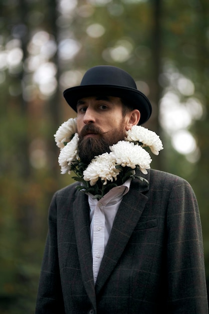 El tema surrealista un hombre barbudo con una chaqueta y un sombrero con un ramo de flores blancas alrededor del cuello