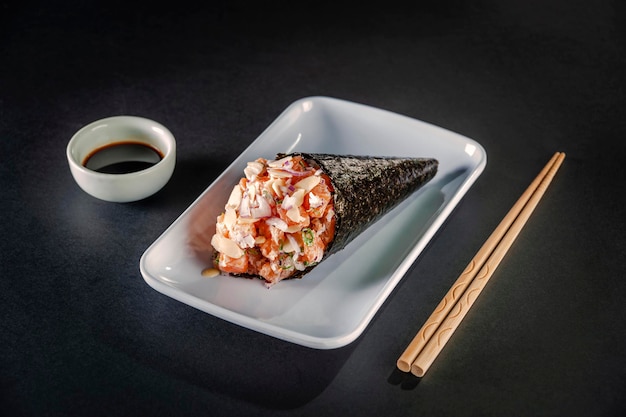 Temaki de salmão com lâminas de amêndoa na chapa branca em fundo preto com molho de soja e pauzinhos