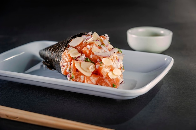 Temaki de salmón con láminas de almendras y cebolla morada sobre un plato blanco de fondo negro.