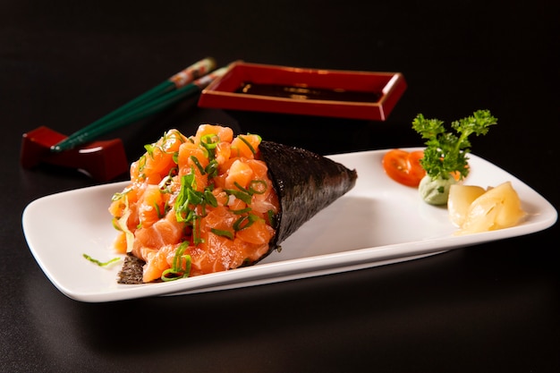 Temaki sushi de salmón en un plato blanco sobre fondo negro.