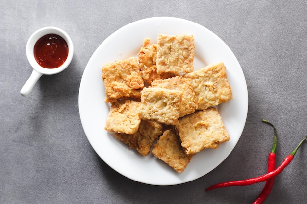 Tempeh frito crujiente en un plato blanco con un fondo gris