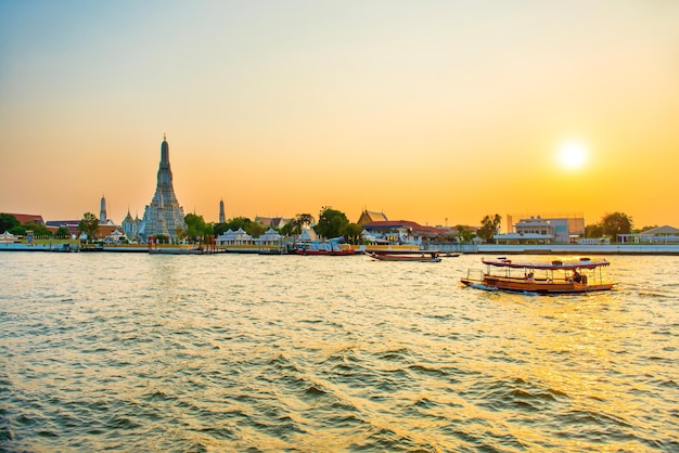 Tempel der Morgenröte oder Wat Arun und Boote am Fluss Chao Phraya bei Sonnenuntergang mit strahlender Sonne Bangkok Thailand