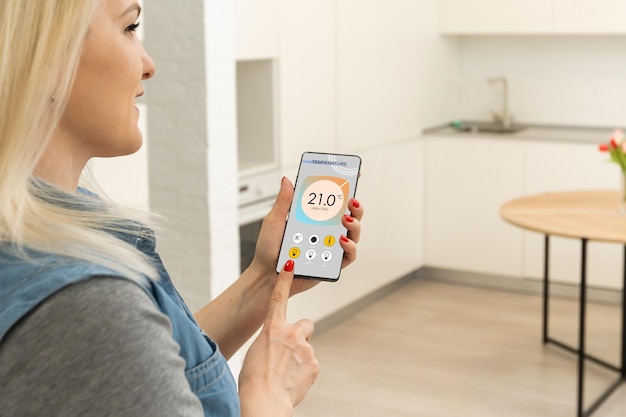 Temperatur-, Sicherheits- und Umgebungskontrolle zu Hause in der mobilen App. Smartphone in Frauenhand. Wohnzimmer im Hintergrund.