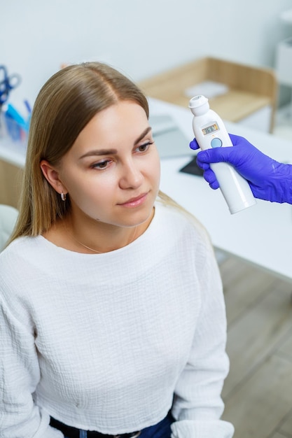 La temperatura de una mujer joven se mide con un termómetro electrónico sin contacto Mujer siendo examinada por un médico