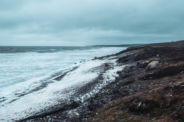 Tempestade na costa do mar branco. Ondas com espuma branca rolam no costão rochoso. Paisagem polar selvagem.