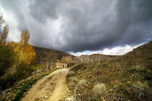 Tempestade no céu com nuvens negras, paisagem de outono, estrada e pequena casa.