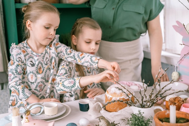 Tempo de férias da páscoa na primavera, família feliz, crianças sinceras, irmãs, meninas, juntas, mãe, divirta-se em casa, decorando a mesa para almoço ou jantar, comida tradicional, decoração festiva da casa