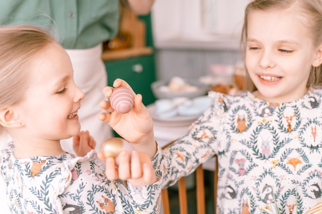 Tempo de férias da Páscoa na primavera, família feliz, crianças sinceras, irmãs, meninas, juntas, mãe, mãe, divirta-se em casa, tradicional, chacoalhando ou despejando ovos, tradição religiosa