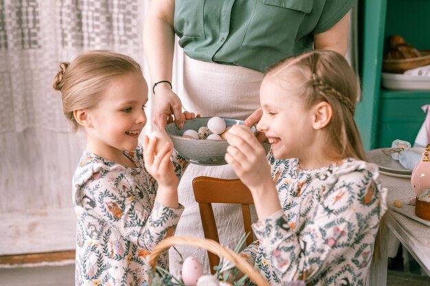 Tempo de férias da Páscoa na primavera, família feliz, crianças sinceras, irmãs, meninas, juntas, mãe, mãe, divirta-se em casa, tradicional, chacoalhando ou despejando ovos, tradição religiosa