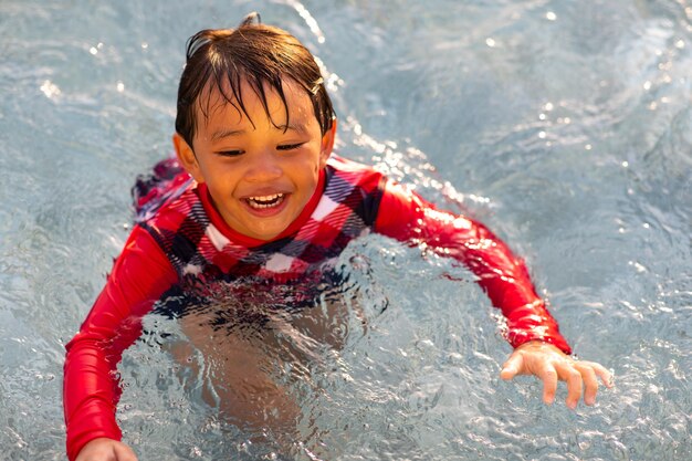 Tempo de férias em família feliz. Menino engraçado asiático espirrando nadando na piscina.