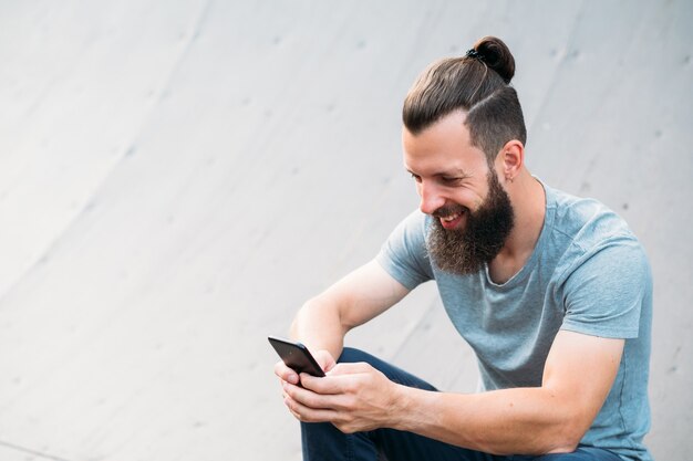 Foto tempo de relaxamento moderno. juventude despreocupada. homem barbudo sorridente navegando no smartphone.