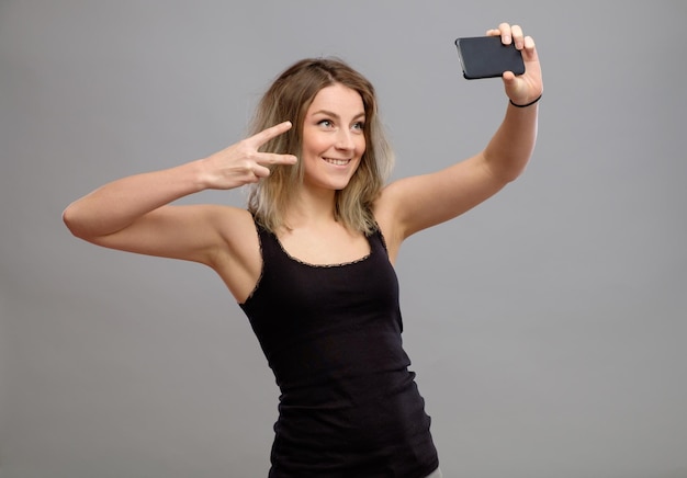 Tempo de selfie Mulheres jovens alegres fazendo selfie com seu telefone inteligente isolado em cinza