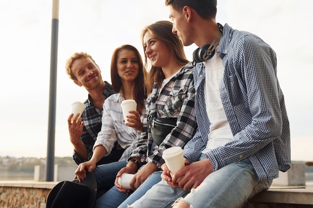 Tempo ensolarado Bebendo café Grupo de jovens amigos alegres que estão ao ar livre se divertindo juntos