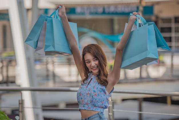 Tempo feliz ao conceito de compra, mulher asiática que guarda sacos de compras e mãos levantadas acima no centro da alameda.