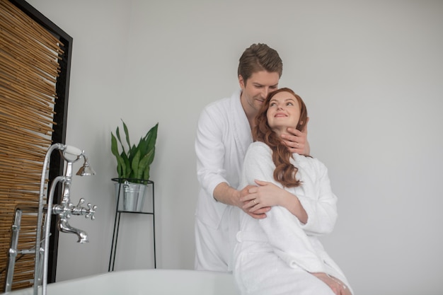 Tempo juntos. Um homem alto de roupão branco abraçando a esposa