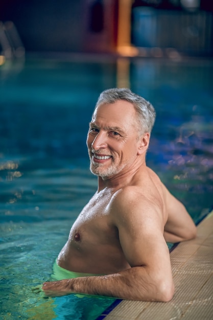 Tempo na piscina. Homem bonito de meia-idade nadando em uma piscina e parecendo satisfeito