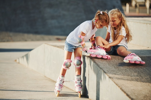 Tempo quente. Na rampa para esportes radicais. Divertem-se duas meninas com patins ao ar livre.