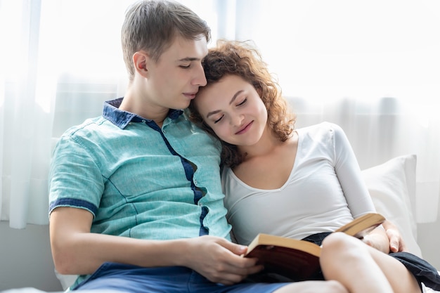 Tempo romântico. Casal da Cáucasia abraça e livro de leitura na cama.