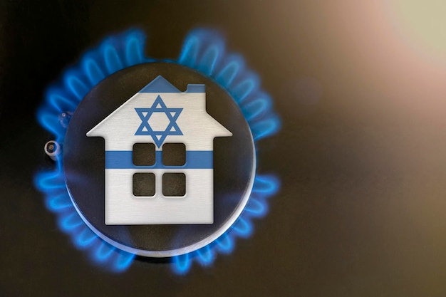 Temporada de calefacción Israel El comienzo de la temporada de calefacción con gas natural El modelo conceptual de una casa se encuentra cerca de la llama de una caldera de gas sobre un fondo negro Costo de calefacción del hogar de Israel