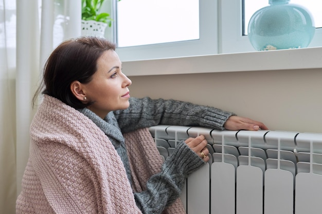 Temporada de aquecimento de inverno Mulher de suéter quente sentada na sala de casa perto do radiador de aquecimento