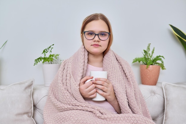 Temporada de inverno frio de outono em casa adolescente sob cobertor sentado no sofá com caneca