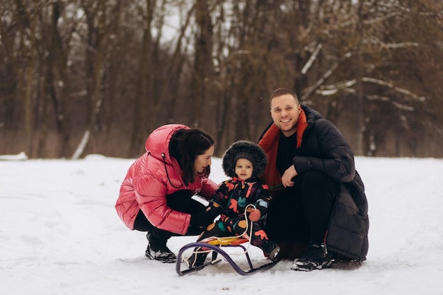 Temporada de paternidade e conceito de pessoas família feliz com criança no trenó andando no inverno ao ar livre
