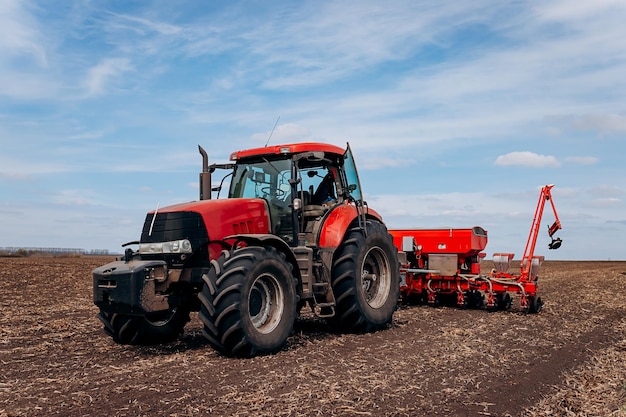 Temporada de semeadura da primavera Agricultor com um trator semeia sementes de milho em seu campo Plantando milho com plantador rebocado Semeadura agrícola O conceito de agricultura e máquinas agrícolas