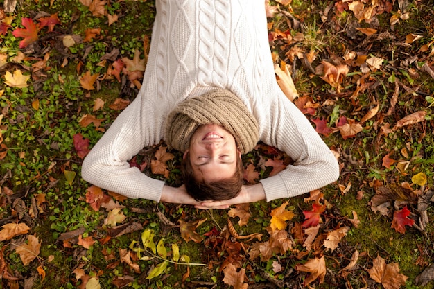 temporada, felicidad y concepto de la gente - joven sonriente tirado en el suelo o hierba y hojas caídas en el parque de otoño