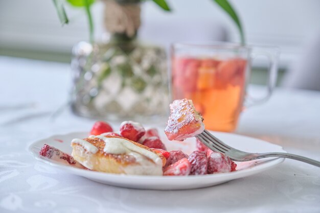 Temporada de fresas, comida y bebida con frutos rojos. Comida en la mesa, panqueques de cuajada con fresas y crema agria. Té con limón y frutos rojos