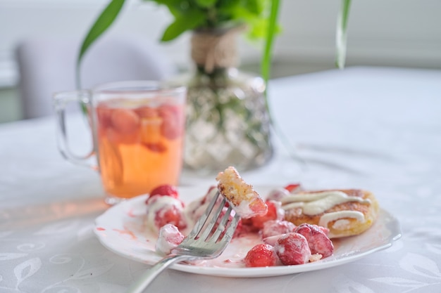 Temporada de fresas, comida y bebida con frutos rojos. Comida en la mesa, panqueques de cuajada con fresas y crema agria. Té con limón y frutos rojos