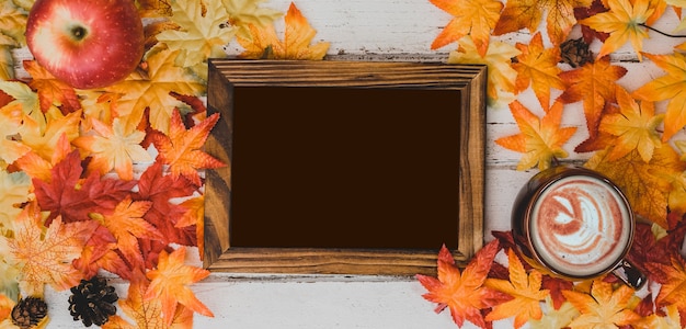 Temporada de otoño y otoño. Chocolate caliente con marco de fotos y hoja de arce falsa sobre mesa de madera. Cosecha cuerno de la abundancia y concepto del día de acción de gracias.