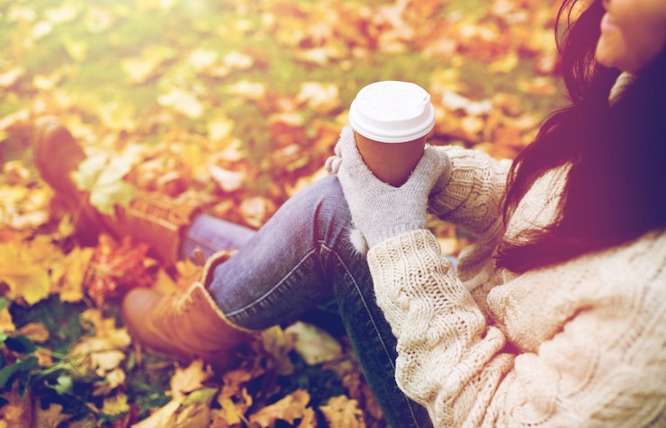 Foto temporada, tecnologia e conceito de pessoas - close de jovem feliz bebendo café de copo de papel no parque de outono