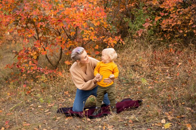 Temporada de vacaciones de Acción de Gracias. Niño con madre al aire libre, fondo de otoño