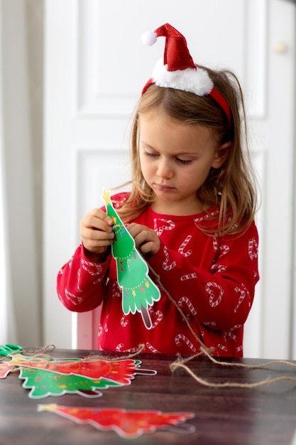 Temporada de vacaciones de invierno Niña linda haciendo adornos navideños guirnalda de árbol de navidad de papel