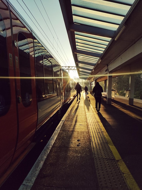Temprano en la mañana en la estación de tren con los pasajeros en silueta por el sol de invierno