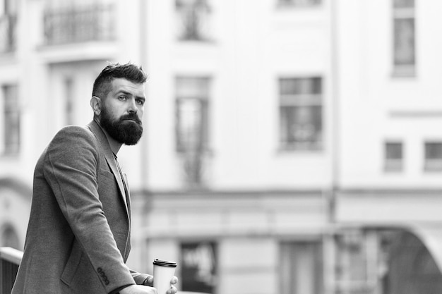 Temprano en la mañana Hipster con vaso de papel caminando en la ciudad Hombre barbudo disfrutando del café de la mañana Empresario en estilo hipster sosteniendo café para llevar El mejor momento del día para tomar café