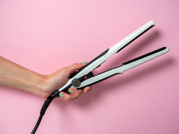 Foto tenaza blanca en la mano de una mujer sobre un fondo pnk. un accesorio para crear peinados. belleza y moda. cuidado del cabello.